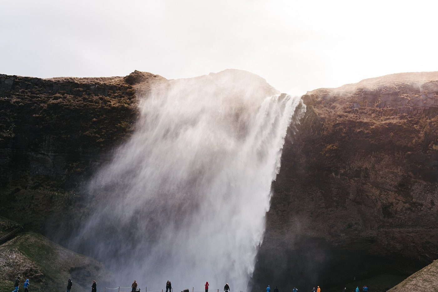 A powerful waterfall falling over a dark cliff in Iceland with people at its base