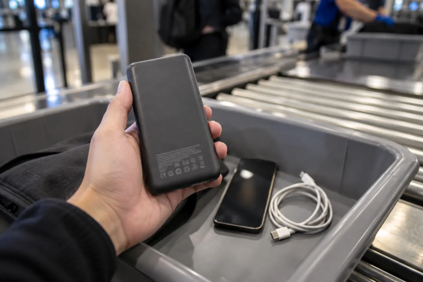 Close-up of the back of a power bank showing a small printed rating label, held in a hand at an airport security tray